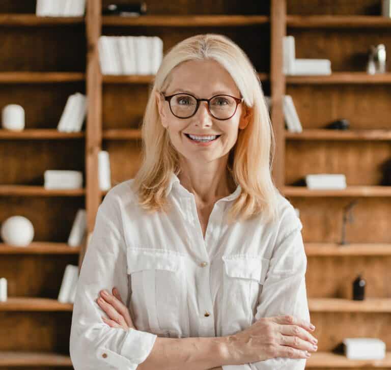 Businesswoman librarian psychologist teacher with arms crossed looking at camera in library office