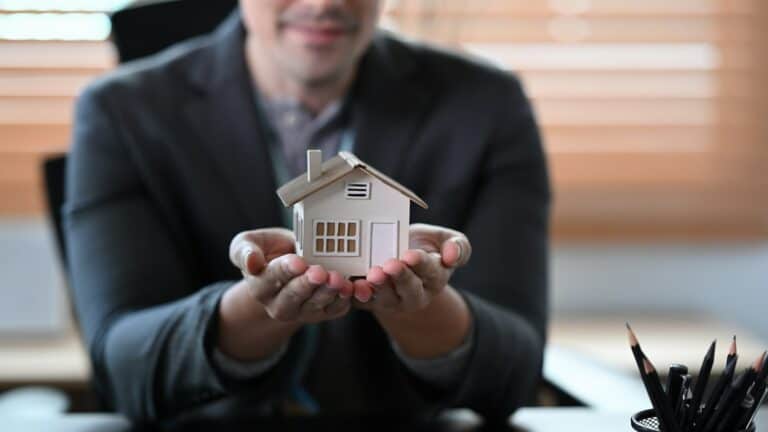 Real estate agent holding small house model. Mortgage and real estate investment concept.