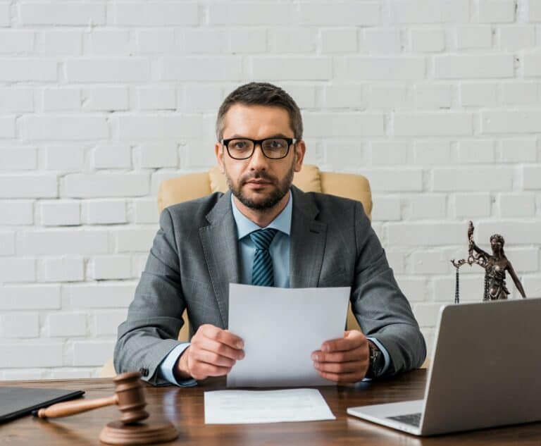 serious lawyer in eyeglasses working with papers and looking at camera in office