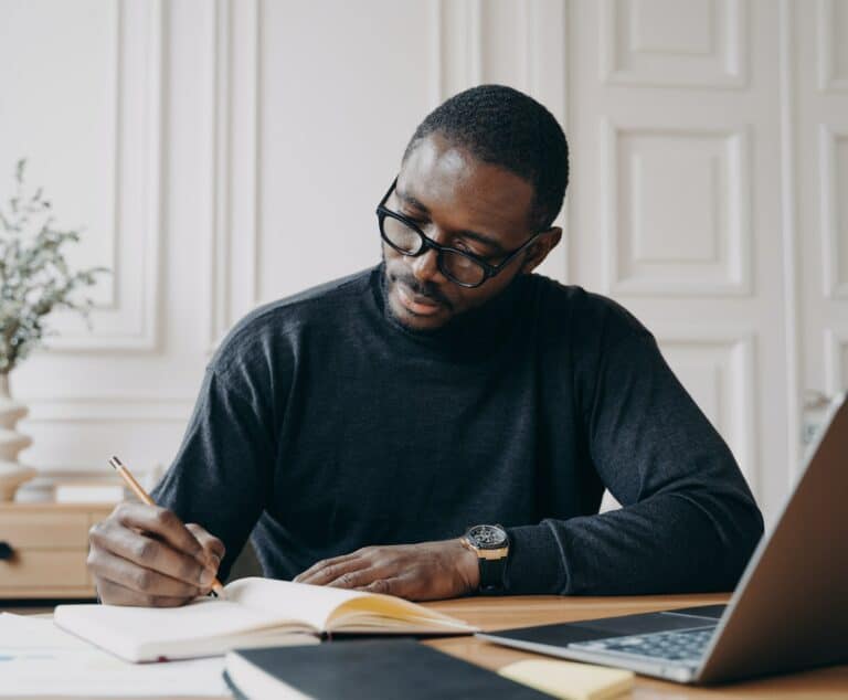 Stunning concentrated Aframerican male lawyer in casual wear making notes in agenda